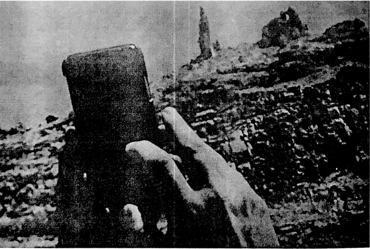 A black and white image of a man's hands pointing a phone towards the site of Lot's wife to take a picture.