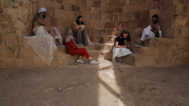 Five people sit on some ancient roman steps near the site of Lot’s cave near Gwar Al Safi in Jordan. Some are writing on pieces of paper and some are gazing into the horizon.