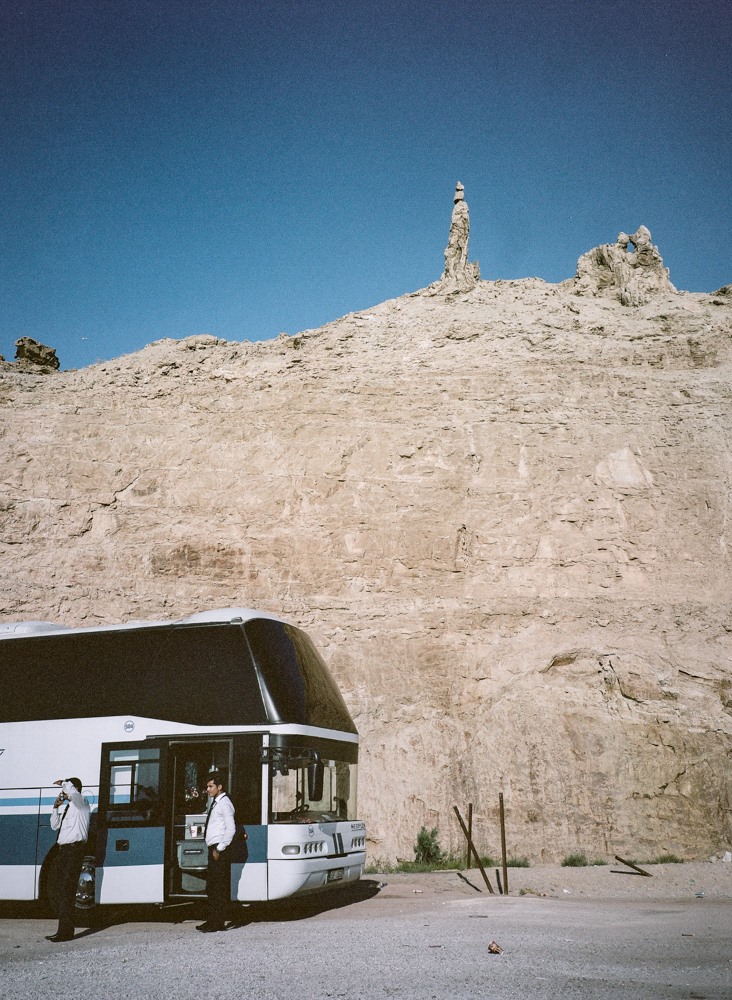 Two tourguids are standing outside a white bus parked on the side of a highway at the site of Lot’s wife near Gwar Al Safi in Jordan.