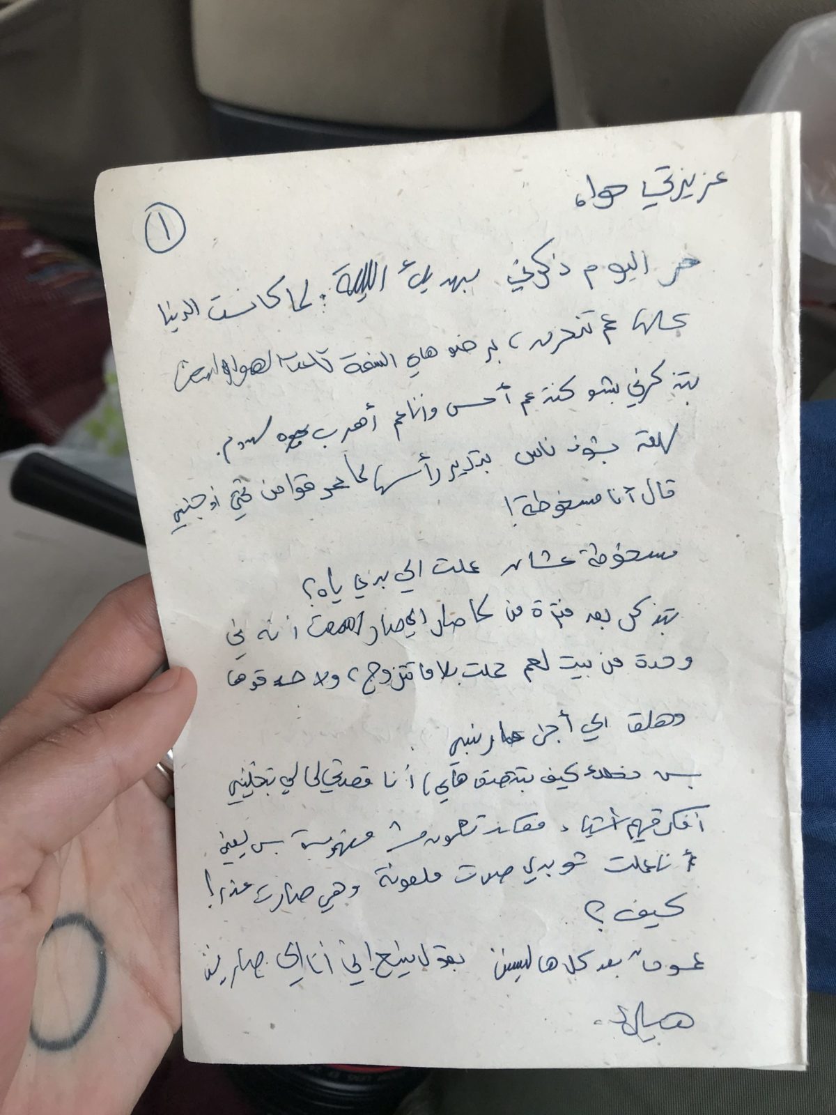 A hand is holding a piece of paper in front of the camera.On the paper, there is a text written in Arabic.