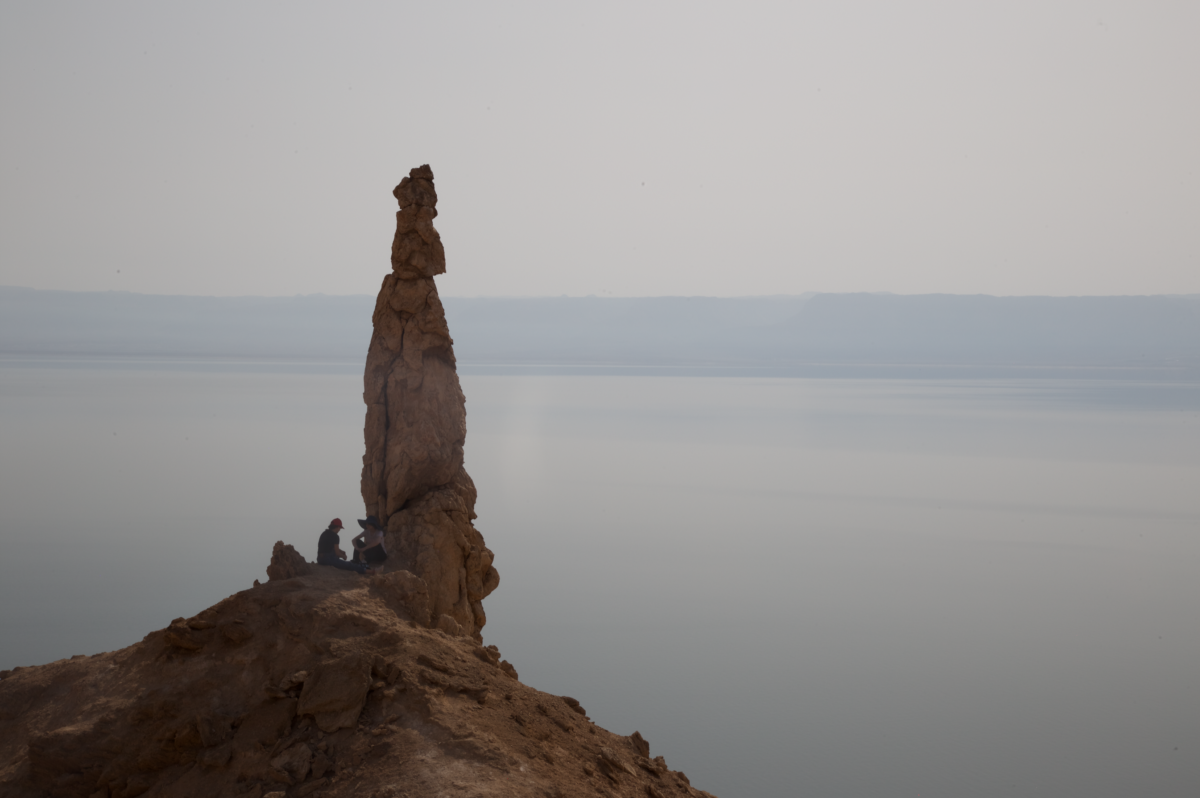 Two girls are sitting next by a large rock on top of a mountain with the Dead Sea in the background. The rock is the site of Lot’s Wife close to Gwar Al Safi in Jordan.